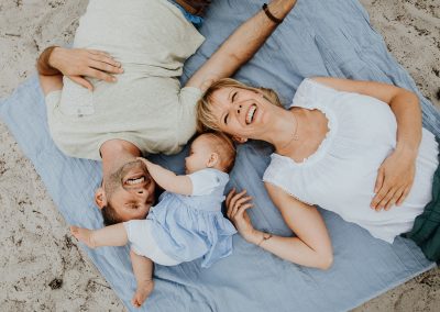Familien Fotografie zeigt glückliches Baby und Eltern auf einer Decke liegend